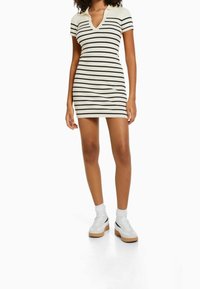 Femme portant une robe courte en côte blanche avec des rayures horizontales noires, des chaussettes blanches et des baskets blanches avec des accents noirs.