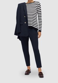 Blazer bleu marine avec boutons dorés, pull rayé noir et blanc, pantalon bleu marine assorti et mocassins marron foncé avec accents dorés.