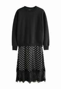 Haut sweat-shirt noir à manches longues, associé à une jupe noire et blanche à pois avec un ourlet en dentelle noire. Les pois sont espacés de manière régulière.