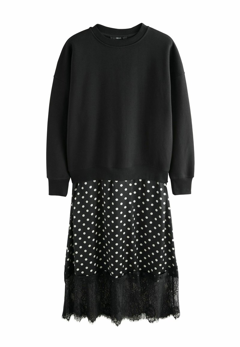 Haut sweat-shirt noir à manches longues, associé à une jupe noire et blanche à pois avec un ourlet en dentelle noire. Les pois sont espacés de manière régulière.