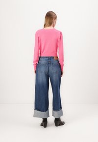 Suéter de punto acanalado rosa con mangas largas y hombros abullonados, combinado con jeans de mezclilla azul de pierna ancha con puños doblados y bolsillos traseros.