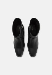 Bocanci din piele neagră, până la gleznă, cu o textură netedă, vârf ascuțit, închidere cu fermoar pe lateral și un design minimalist. Branding-ul este vizibil pe branț.