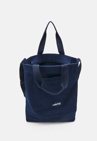 Navy denim tote bag with dual handles, featuring a front pocket and a subtle logo. Sturdy fabric with a clean, simple design.