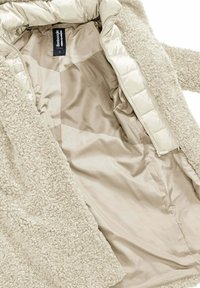 Beige, pluizige fleece buitenlaag met een gladde, glanzende voering. Heeft een volledige rits en een label aan de binnenkant. Gestructureerde en zachte uitstraling.