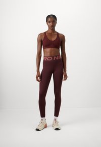 Soutien-gorge de sport bordeaux avec un motif discret, associé à un legging assorti avec une large ceinture logo. Chaussures de sport beiges et marron.