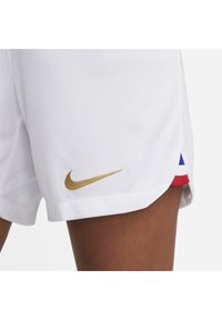 Shorts de sport blancs avec un logo Nike doré sur l'ourlet gauche et des accents rouge, blanc et bleu sur les fentes latérales. Tissu doux au toucher.