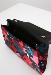 Pestrá látková kabelka do ruky s výrazným květinovým vzorem v červené, růžové, modré a černé barvě. Vnitřek obsahuje kapsu na zip a zapínání na klopu.