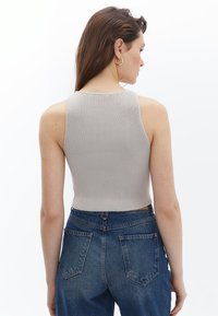 Světle šedý žebrovaný top s přiléhavým střihem, spárovaný s modrými džínami s vysokým pasem, zobrazený zezadu.