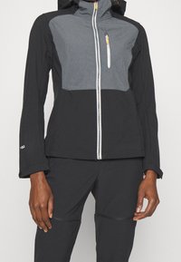 Veste zippée noire et grise avec capuche, dotée de poignets élastiques, d'une poche poitrine et d'un panneau supérieur texturé. Tissu léger.