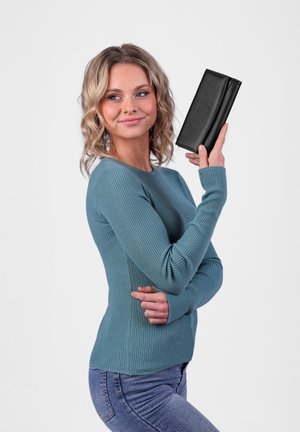 Black leather wallet with a smooth texture, held in a hand. The person is wearing a ribbed teal sweater and jeans.