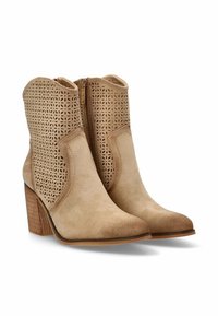 Botines de ante beige con un patrón floral recortado, punteras puntiagudas y tacones de madera apilada. Cierre lateral para facilitar su uso.