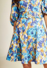 Blumenmuster-Kleid in Blau, Gelb und Weiß. Hat ein tailliertes Oberteil, voluminöse Ärmel und einen breiten Gürtel mit einer runden Schnalle.
