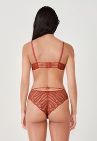 Ensemble de lingerie en dentelle rouge mettant en avant des motifs complexes, des bretelles réglables et une fermeture décorative à crochet sur le soutien-gorge et le slip.