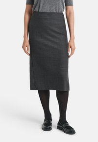 Jupe à carreaux noir et blanc, longueur genoux, en tissu lisse. Associée à des collants noirs et des mocassins. Design simple et ajusté.