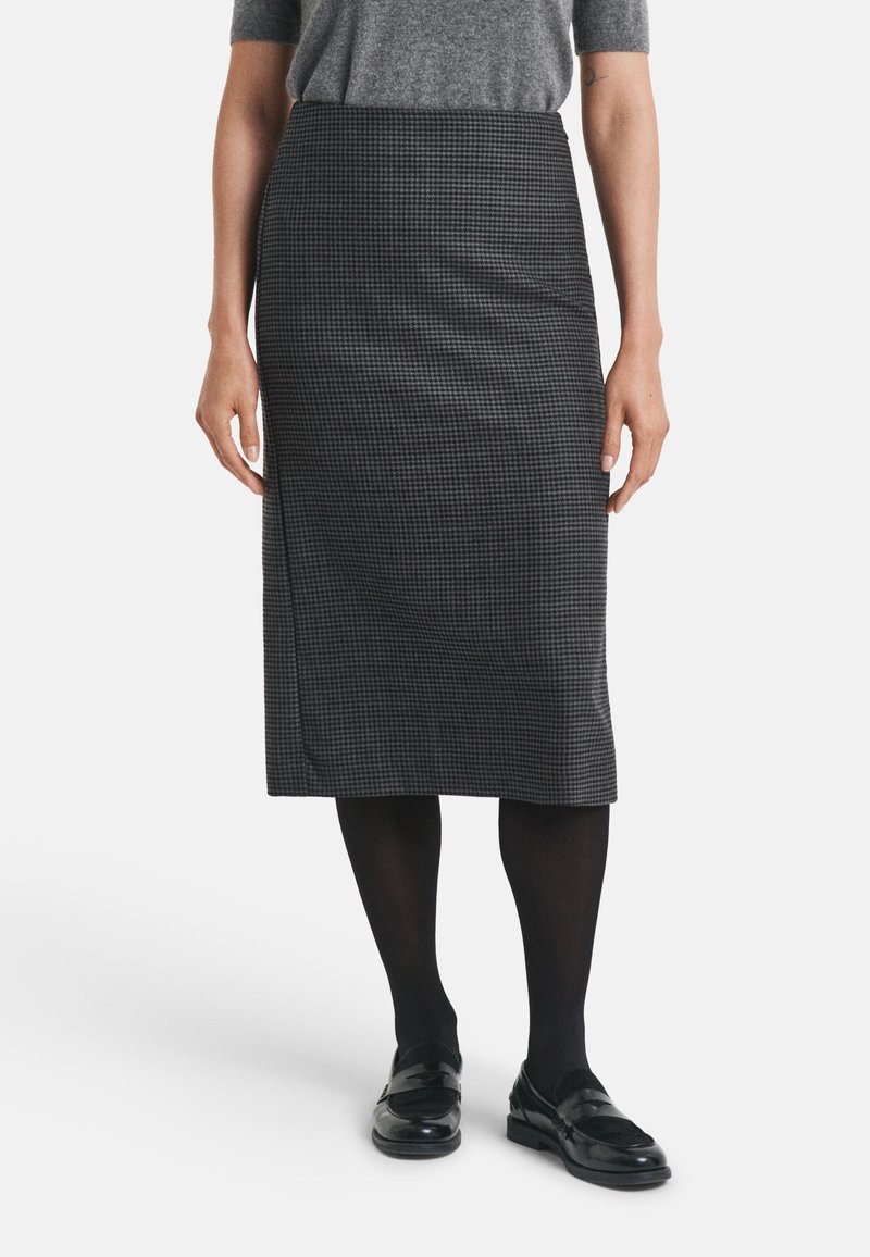 Jupe à carreaux noir et blanc, longueur genoux, en tissu lisse. Associée à des collants noirs et des mocassins. Design simple et ajusté.