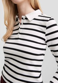 Gestreepte lange mouwen polo in wit en zwart, met een platte kraag, een drie-knoopsluiting, geribde textuur en een getailleerde pasvorm.