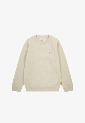 Pull en tricot beige avec un col rond, des longues manches et un petit patch d'ours sur la poitrine. Comprend une étiquette de marque jaune sur le côté.