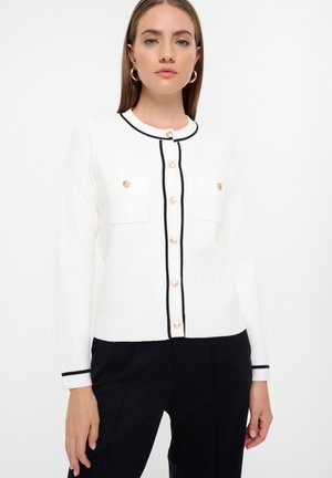 Cárdigan blanco de punto con ribete negro, con botones en tono dorado y dos bolsillos frontales. Textura suave y diseño entallado.