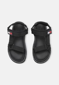 Svarta sandaler med justerbara nylonremmar, texturerade sulor och gummikanter. Har en liten logopatch i rött, vitt och blått.