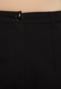 Pantalon noir à la texture lisse, doté d'une fermeture à bouton à l'avant, de passants pour ceinture, et d'une coupe droite le long de la jambe.