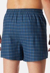 Boxers à carreaux bleus avec une taille élastique. Le tissu a une texture lisse, avec un motif en grille comportant des lignes grises.