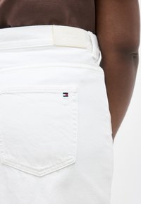 Κοντινή λήψη πίσω τσέπης λευκού τζιν με μικρό λογότυπο σημαίας Tommy Hilfiger και δερμάτινο λογότυπο πάνω στη μέση.