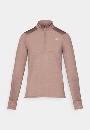 Dolga športna majica v prašnem rožnatem odtenku z ovratnikom na pol zadrgo, teksturirano blago in temnejšimi poudarki na ramenih. Logotip New Balance na prsih.