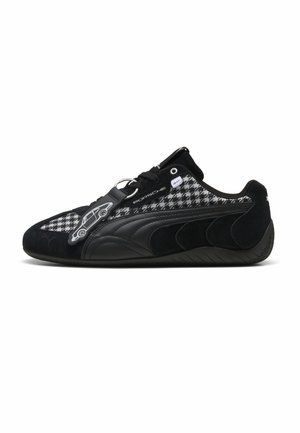Schwarzer Sneaker mit grau-weiß kariertem Einsatz, Porsche-Logo, Leder- und Wildlederdetails sowie einem kleinen autoschlüsselanhänger an den Schnürsenkeln.