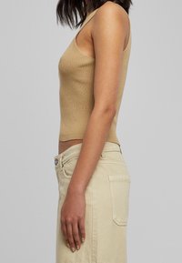 Beżowy prążkowany top na ramiączkach wąskich, zestawiony z wysokim stanem jasnobeżowych spodni. Tkanina wydaje się miękka i ma teksturowane wykończenie.