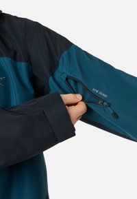 Waterdichte jas met een zwart en teal ontwerp, elastische manchetbanden en een ritszak op de linkermouw met "STX 20.000" detail.
