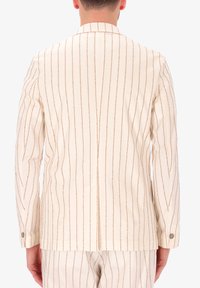Giacca a righe crema con pinstripe marroni verticali, colletto classico e polsini con bottoni. La texture del tessuto appare liscia.