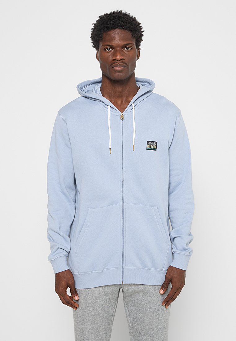 Hellesblauer Reißverschluss-Hoodie aus weichem Stoff. Verfügt über eine Fronttasche und Kordelzüge mit goldenen Spitzen. Kleines Markenlogo auf der linken Brust.