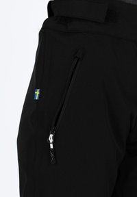 Pantalons noirs en tissu doux et extensible, dotés d'une poche zippée et d'un petit détail de drapeau bleu et jaune sur le côté.