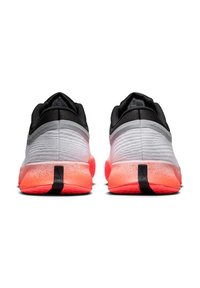 Ein Paar weiße und schwarze Sportschuhe mit leuchtend pinken gesprenkelten Sohlen, von hinten auf einem weißen Hintergrund betrachtet.