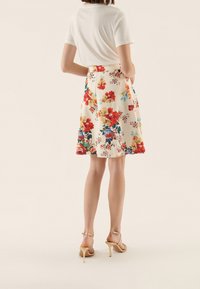 Blommig kjol med krämfärgad bakgrund, prydd med röda och blå blommor. A-linjeformad, knälång, ihop med beige sandaler med remmar.