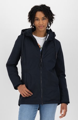 Veste à capuche marine avec un motif texturé, fermeture éclair avant, cordon de serrage réglable et poches latérales, portée sur un T-shirt léger et un jean.