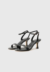 Sandales à talons en cuir noir avec deux brides avant, des brides de cheville, un talon fuselé et une texture lisse. Design élégant dans un style minimaliste.