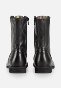 Botas de tobillo de cuero negro con una textura suave, puntera redonda y cremallera en la parte trasera. Cuentan con un forro a cuadros y un tacón bajo y plano.