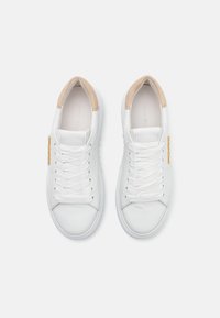 Adidași din piele albă cu vârful rotund, accente de suede crem la călcâi și șireti albi. Prezentare cu un tag logo auriu pe lateral.