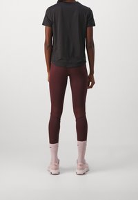 Černé tričko s krátkým rukávem, vínové legíny s průsvitnými panely, světle růžové ponožky a obuv. Oblečení má přiléhavý střih.