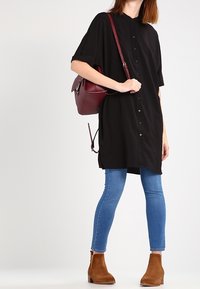 Musta napillinen mekko, jossa on lyhyet hihat, päällä vaaleansiniset tiukat farkut ja ruskeat nilkkurit, sekä burgundinvärinen käsilaukku.