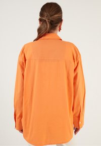 Långärmad, oversized skjorta i klarröd bomull, med spetsig krage, knappade manschetter och ett bakstycke med detaljer.