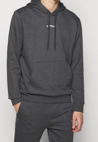 Felpa grigia con cappuccio, tasca frontale, cordini e dettaglio del logo. Realizzata in un tessuto morbido con polsini e orlo a costine.