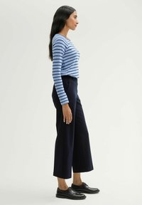 Gestreepte blauwe longsleeve top met marineblauwe wijde broek en zwarte schoenen, zijwaarts weergegeven tegen een neutrale achtergrond.