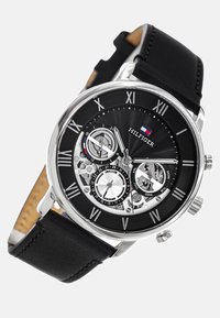 Orologio con cinturino in pelle nera e cassa argentata, caratterizzato da un quadrante nero testurizzato, numeri romani e più sub-quadranti per la data e l'ora.