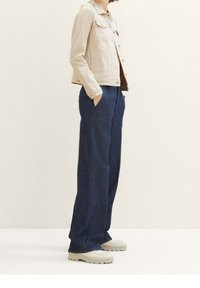 Beige denim jacket with a collar, paired with dark blue wide-leg pants. Footwear is cream-colored with a textured sole.