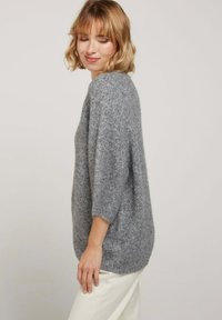 Pull en maille gris avec des manches courtes, une coupe ample et une texture douce. Présente des manches raglan et un col rond.