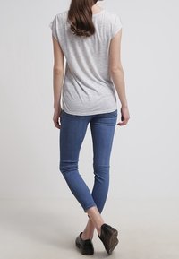 Světlé šedé tričko s krátkým rukávem a volným střihem, spárované s tmavě modrými skinny džíny a černými botami, viděné ze zadu.
