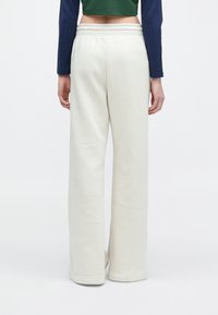 Fehér, bő szárú melegítőnadrág puha anyagból, rugalmas derékkal, egyszerű, sima textúrával, minta vagy díszítés nélkül.