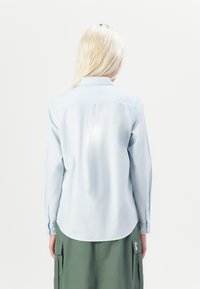 Helles blaues Langarmhemd mit Kragen und Knopfmanschetten, mit einem abgerundeten Saum und glatter Textur. Getragen mit grünen Cargo-Hosen.